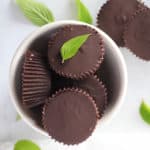 White bowl full of chocolate peppermint cups with mint leaves surrounding.