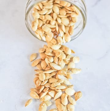 Roasted squash seeds pouring out of a clear jar.