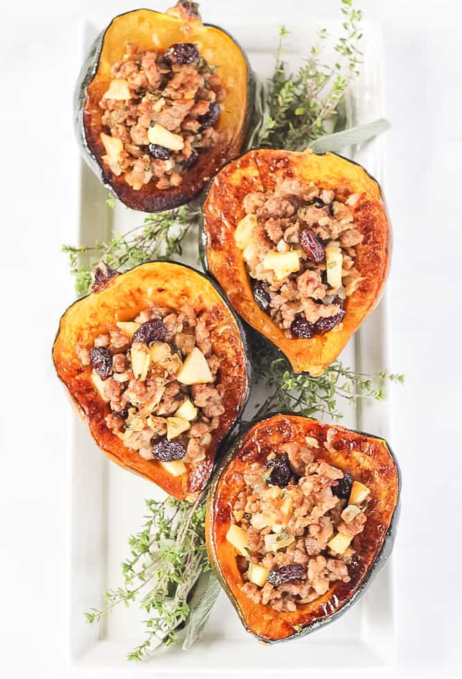 Stuffed Acorn Squash filled with sausage, apples and cranberries on a white serving plater with herbs.