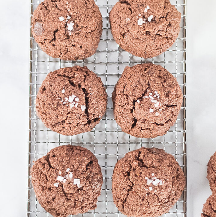 Six dark double chocolate hazelnut cookies on a cooling rack topped with salt.