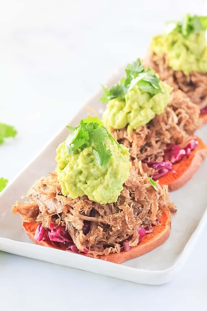 Sweet potato bun sliders with carnitas served open faced on a white platter.