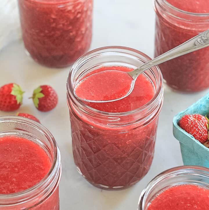 Half pint glass ball mason jars filled with no-cook strawberry honey freezer jam.