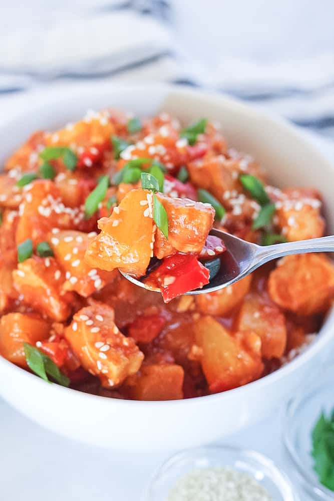 Spoonful from white bowl full of healthy sweet and sour chicken.