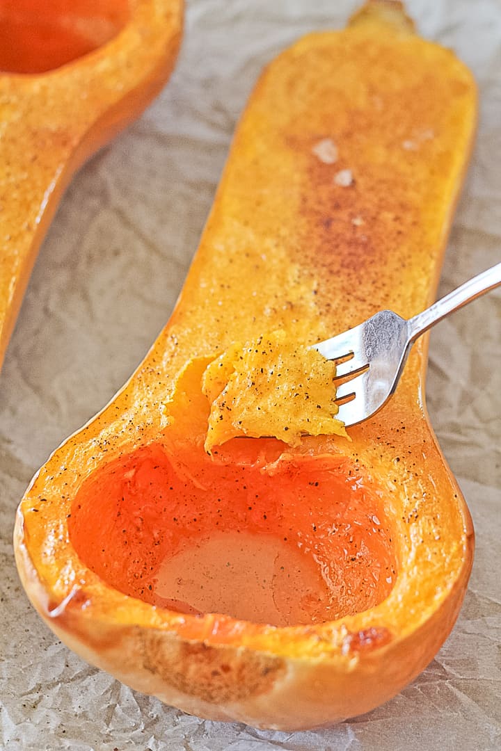 Oven roasted butternut squash cut in half with a fork scooping a bite.