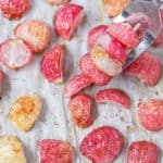 Roasted radishes on a sheet pan with several stacked on a fork.