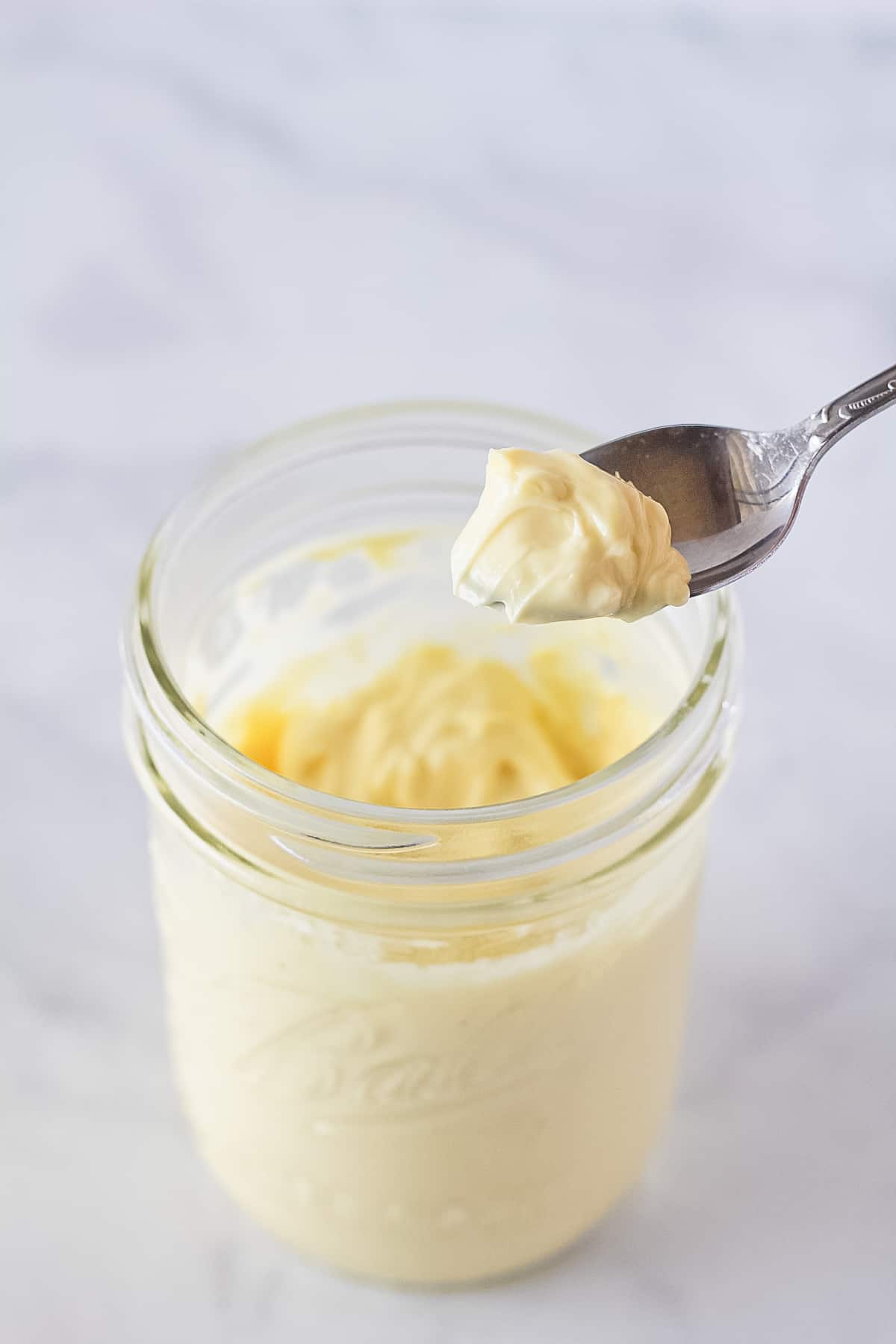 Homemade Mayo being scooped out of a mason jar with a spoon.