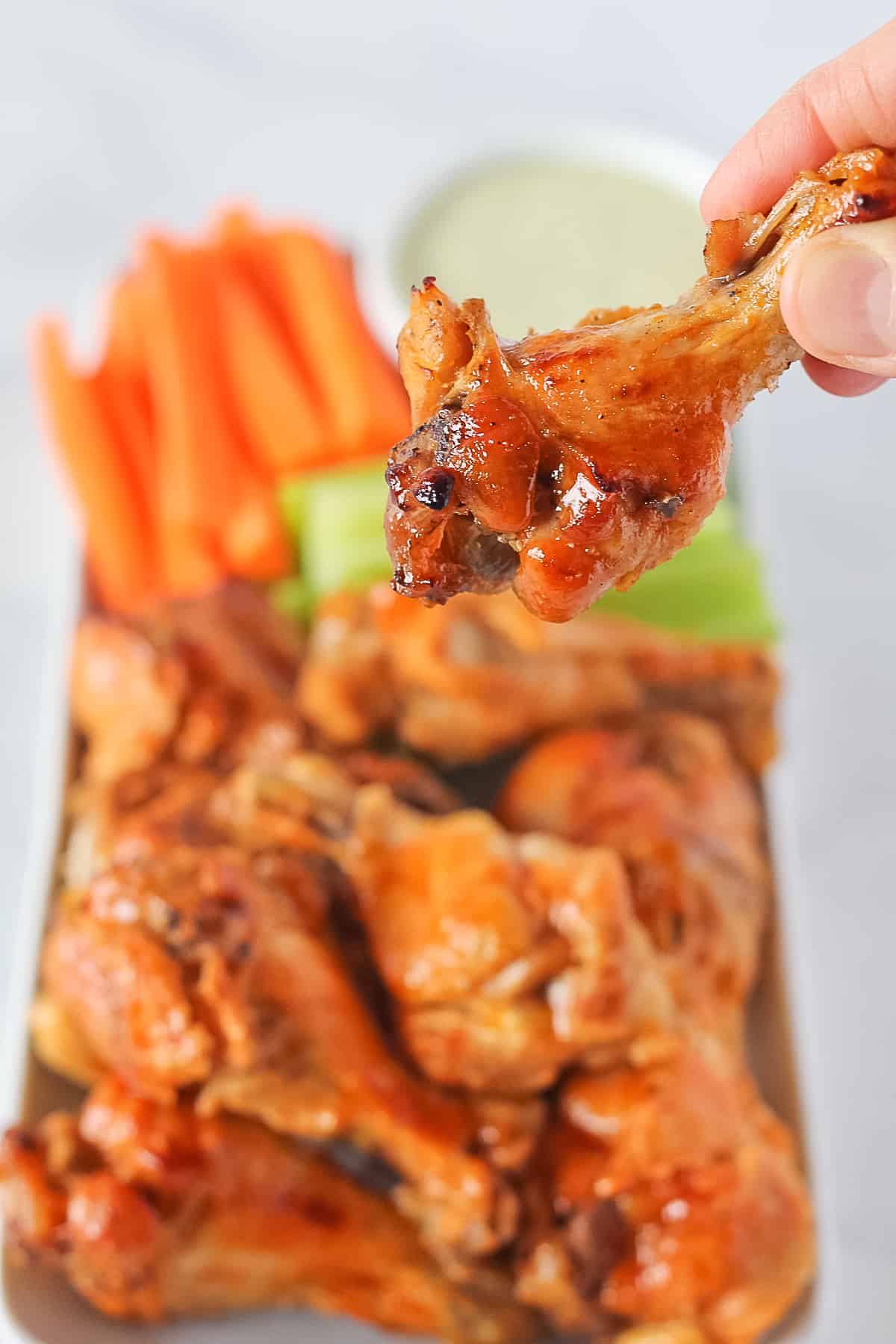 Instant Pot Chicken Wings, one wing being picked up, on a white serving plate with carrots, celery and homemade ranch dressing.