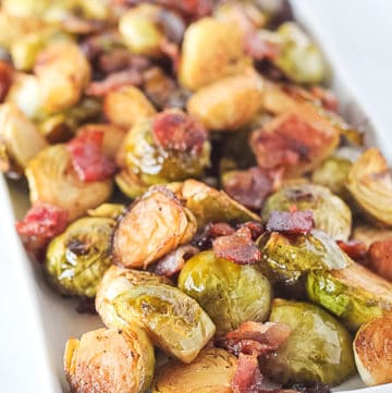 Roasted Brussels Sprouts with bacon on a white serving dish.