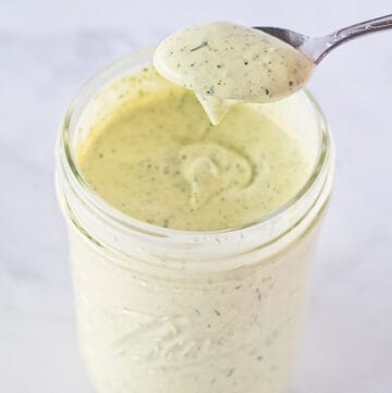 Homemade ranch dressing being scooped with a spoon from a mason jar.