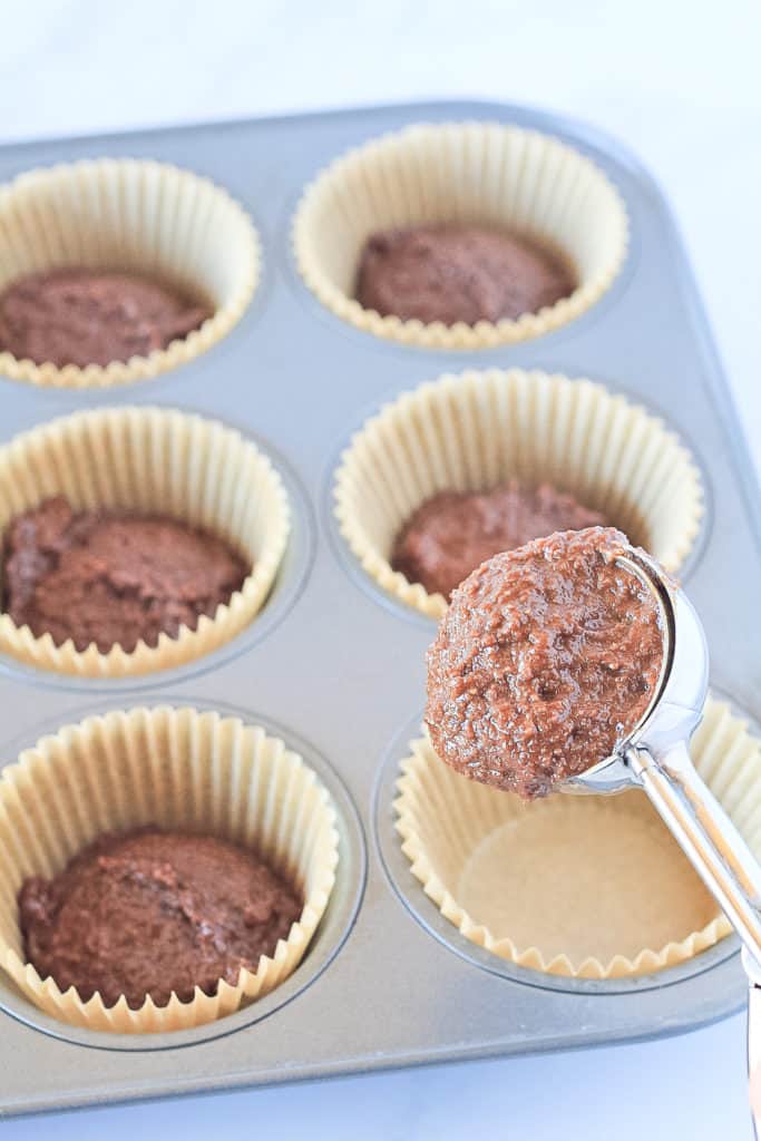 Chocolate cupcake batter being portioned into the muffin pan with a cookie scoop.