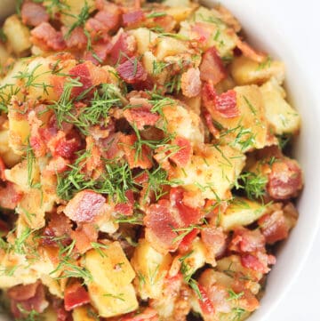 Close up of half of a white serving bowl filled with Hot German Potato Salad topped with bacon and dill.