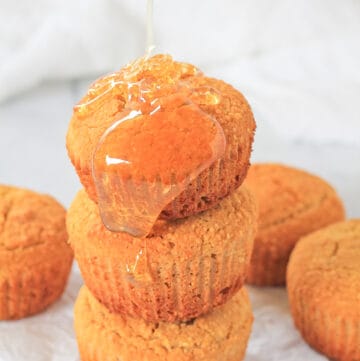 Stack of three gluten free cornbread muffins with honey being poured over top of them.