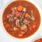 Stew with vegetables, meat and thyme in a white bowl.