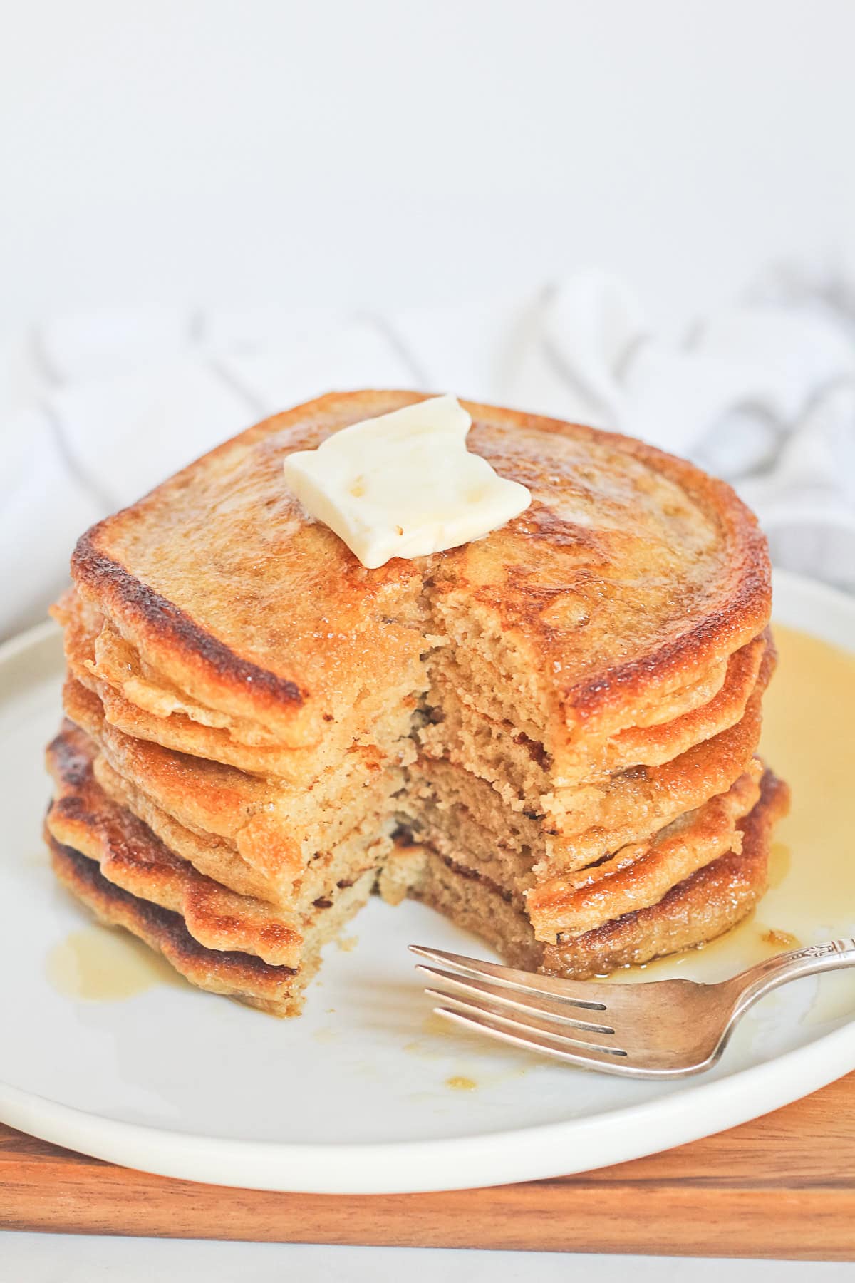 Stack of einkorn pancakes on a white plate with butter, syrup and fork.
