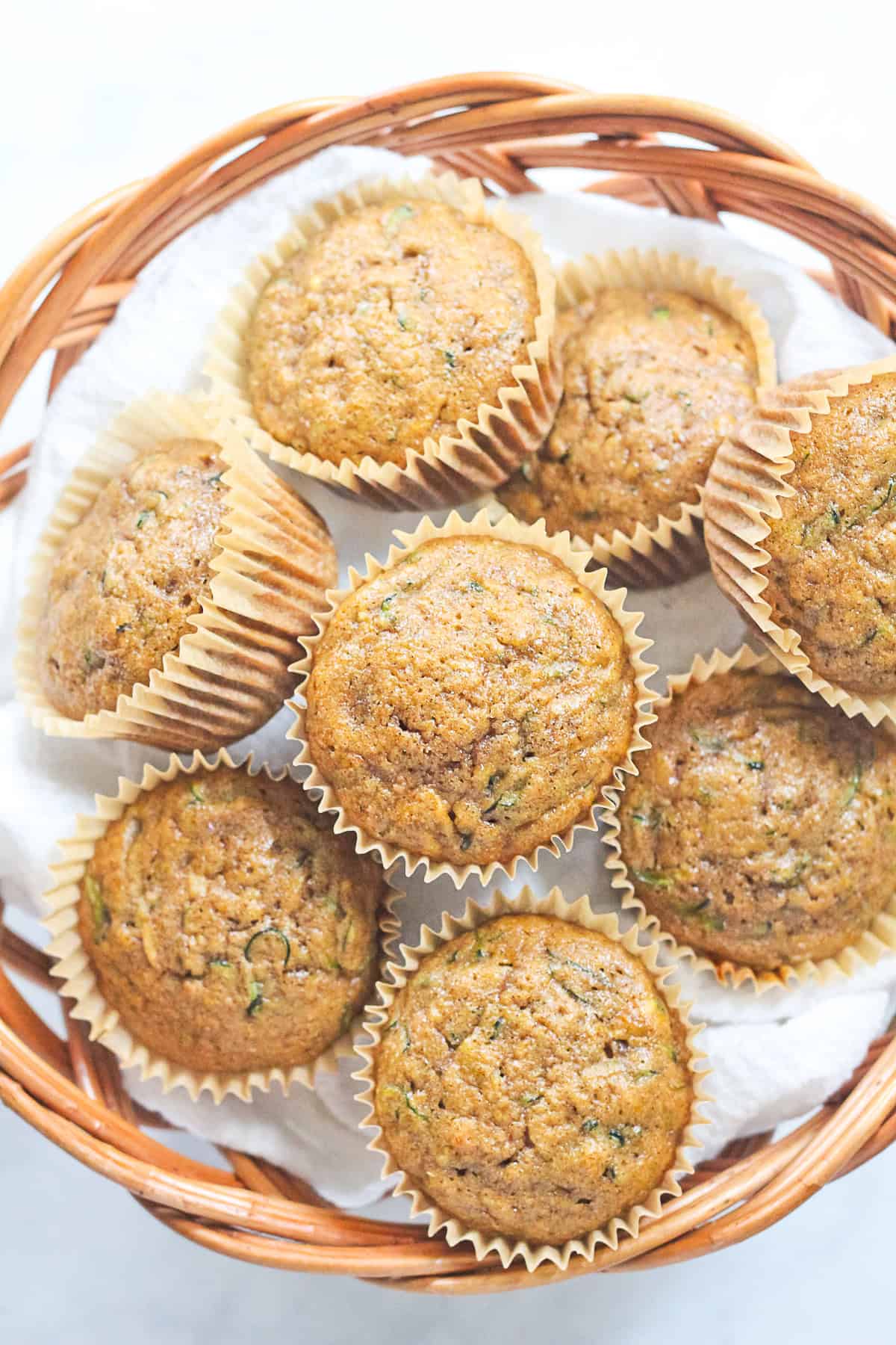 Zucchini muffins in a basket with white towel.