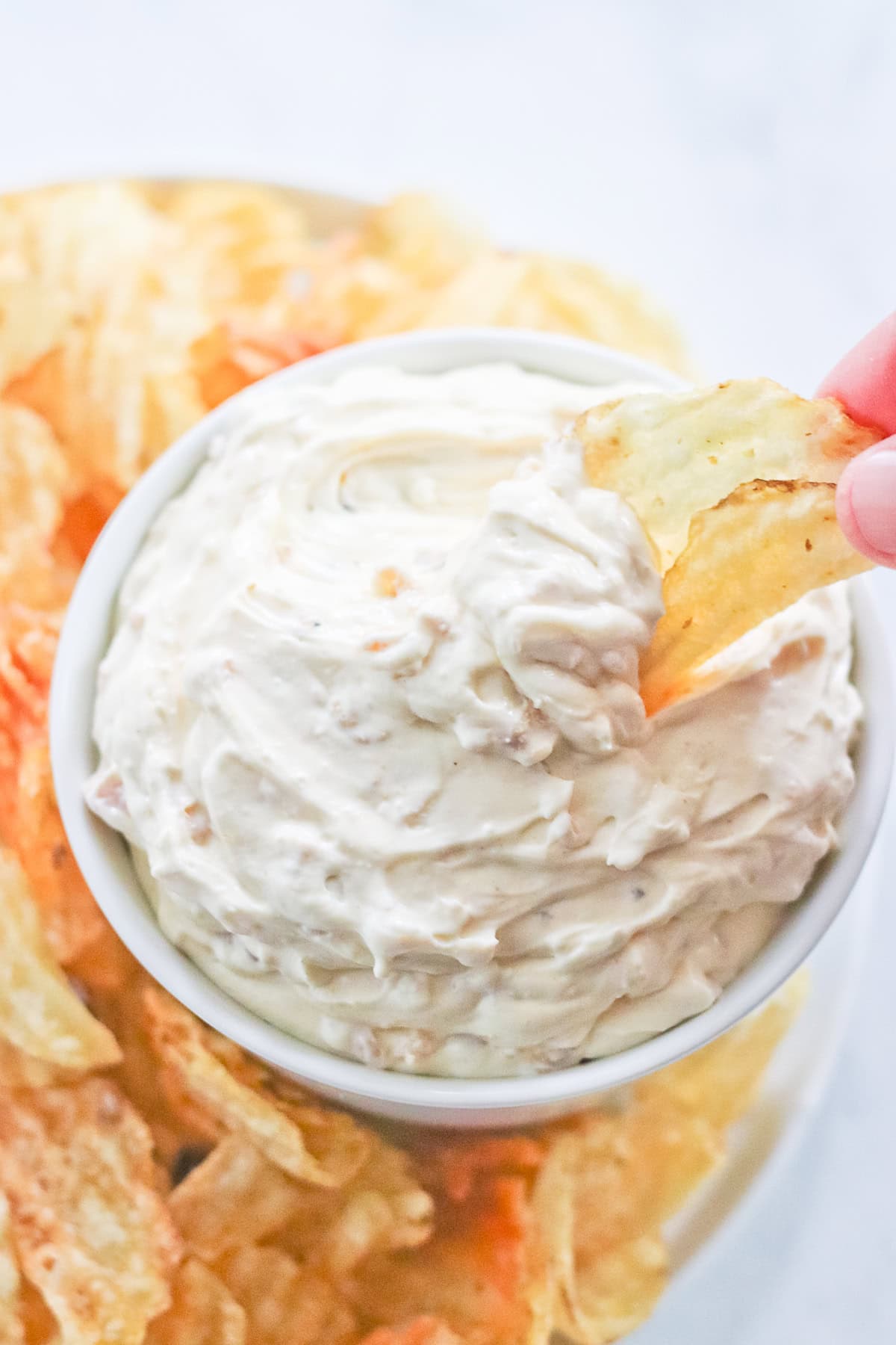 Potato chip being dipped into a bowl of clam dip.