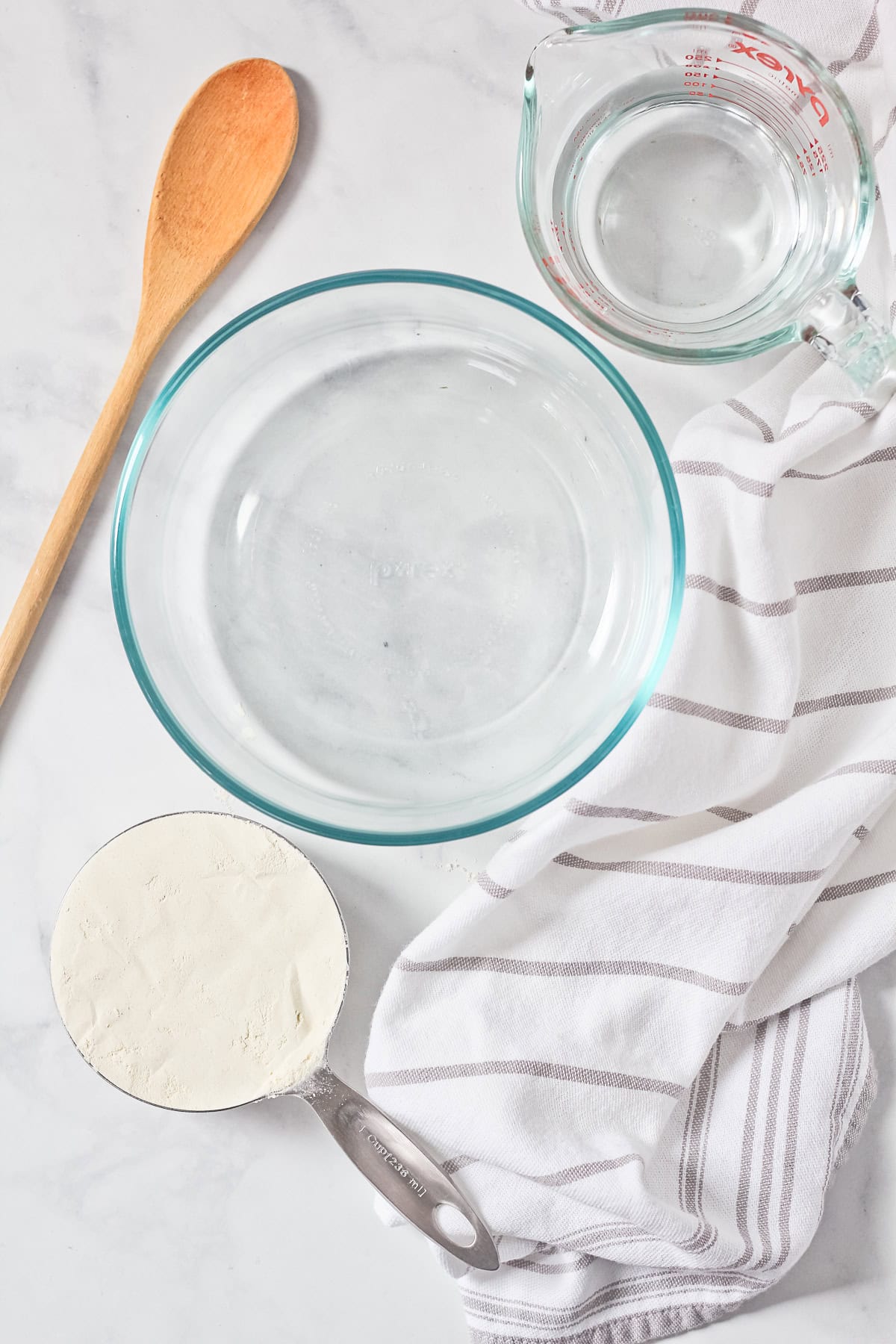 Ingredients of glass bowl, wooden spoon, flour and water to make homemade sourdough starter.